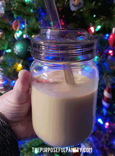 Canning jar with coffee lid and straw in front of Christmas tree full of cinnamon eggnog. Repurposing canning jars.