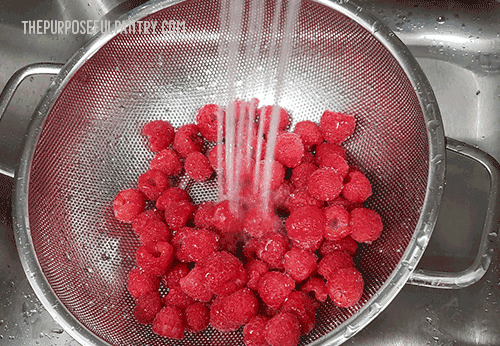 Red Raspberries in a colander, in the sink, being rinsed by the faucet.