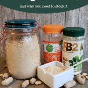 Glass jar full of peanut butter powder and dish with powder on wooden background with peanuts strewn around