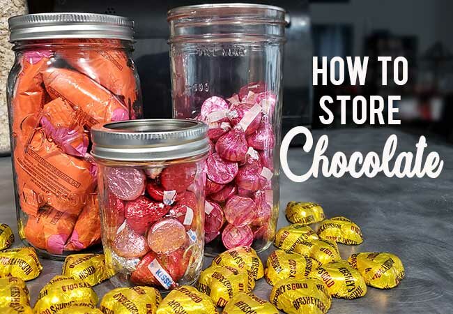 Three mason jars full of Valentine's Day chocolate candies on a gray kitchen counter with heart-shaped chocolate candies scattered to learn to store chocolate