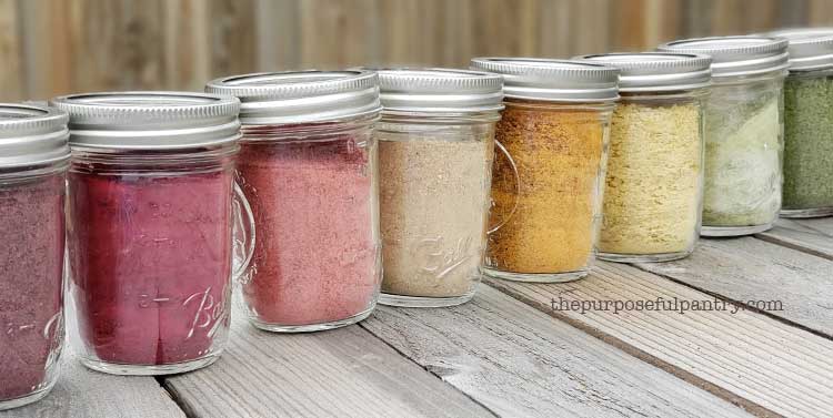 row of jars of dehydrated fruit and vegetable powders on picnic table.