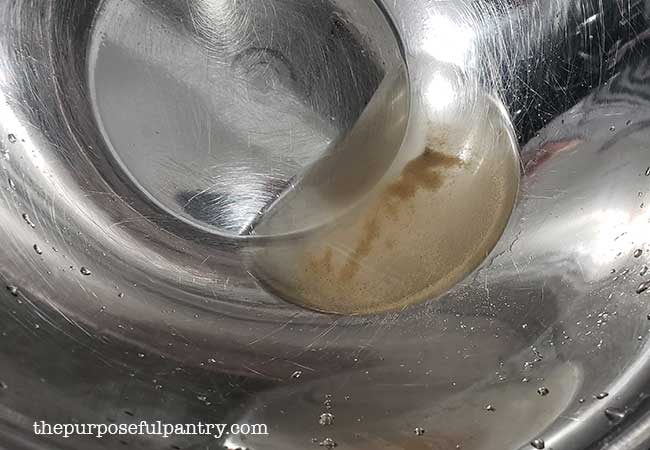 Stainless steel bowl showing the amount of sand left after washing leaves to prepare for dehydrating radishes and leaves