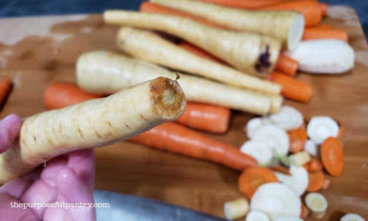 Wooden cutting board with cut parsnips and carrots in preparation to be cut into coins