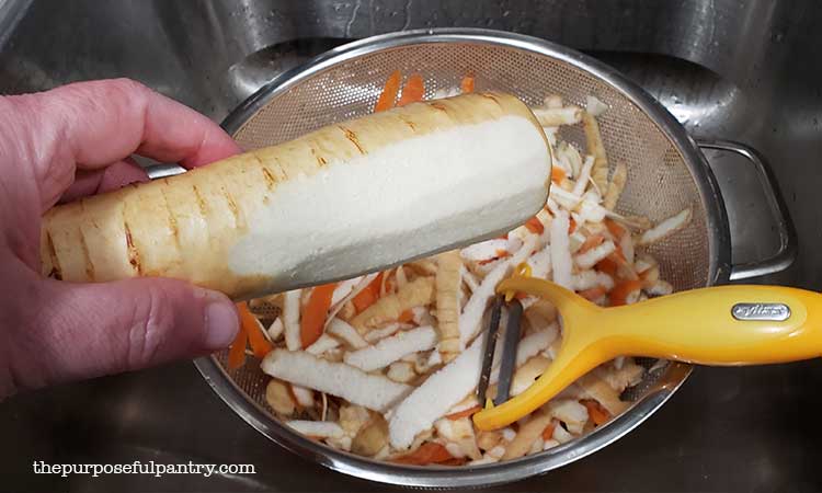 Steel colander with peeler and a partically peeled parsnip to be dehydrated.