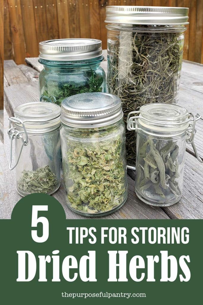 Mason jars for storing dried herbs on a picnic table in front of a rust colored fence.