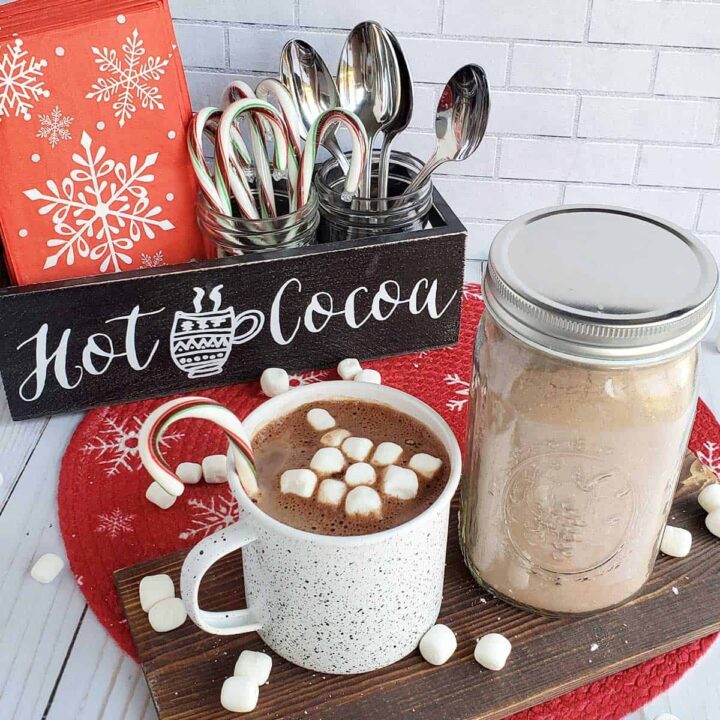 Hot cocoa mix in a jar with a cup of hot cocoa and decorated table.
