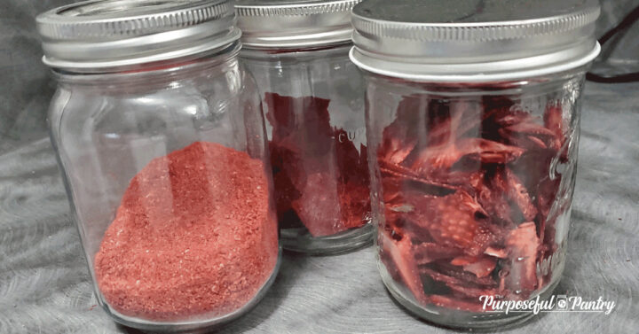 3 Mason jars of strawberry powder, strawberry fruit leather bits and dehydrated strawberries on gray countertop