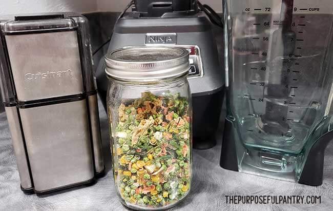 Jar of finished dehydrated mixed vegetables in front of grinder and blender