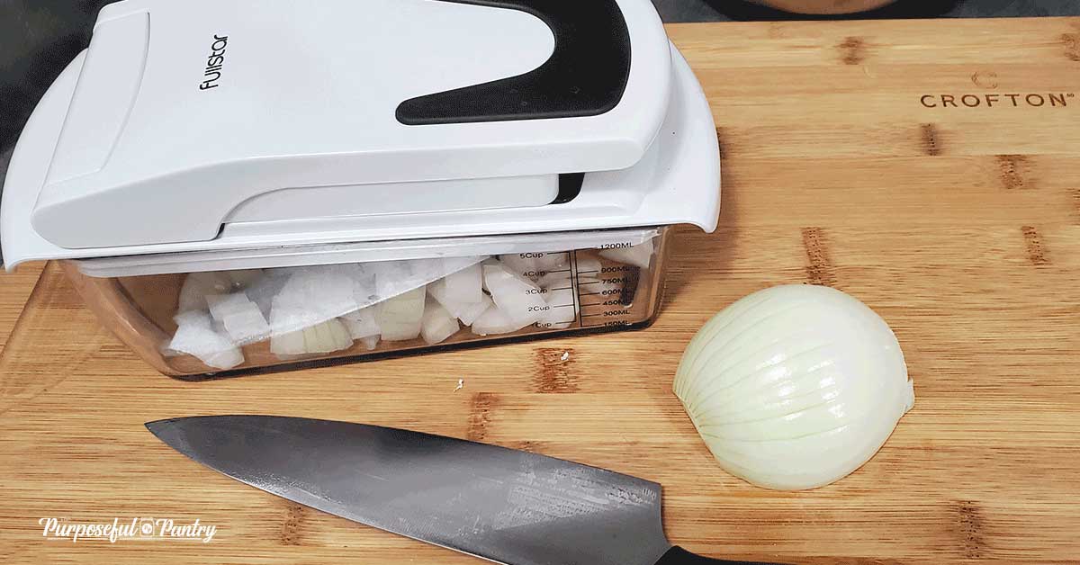 Fullstar Vegetable Chopper, knife, and onion on a wooden cutting board for dehydrating
