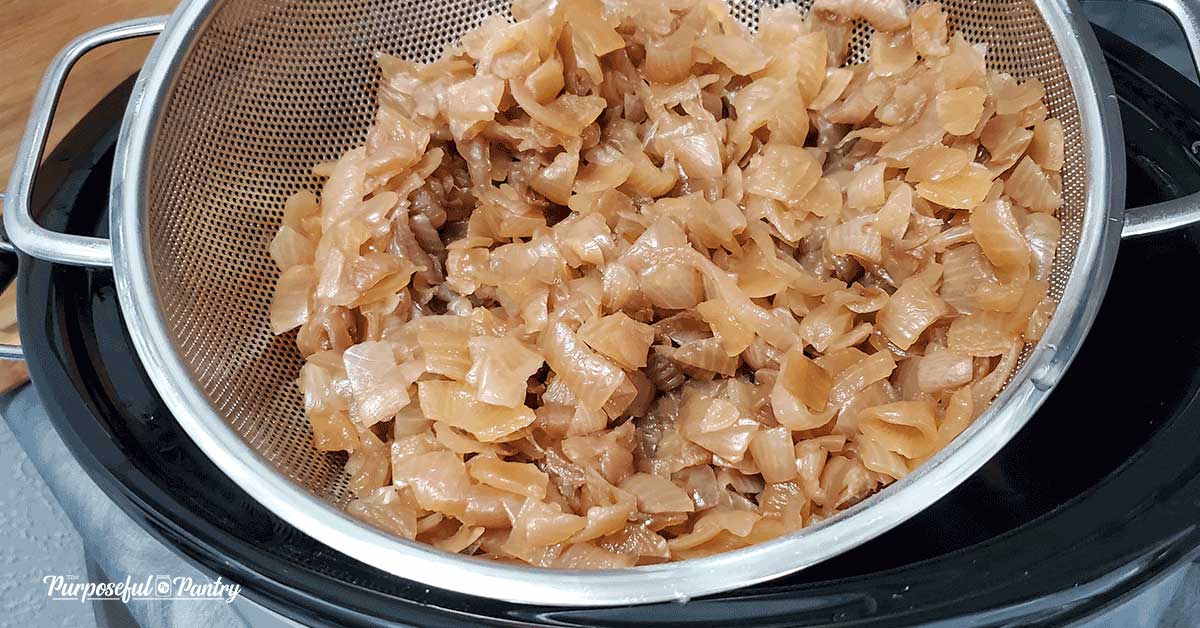 Stainless steel mesh strainer full of caramelized onions getting read for dehydrating