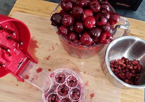 Bowls of fresh cherries and a 6 part cherry pitter on a wooden surface