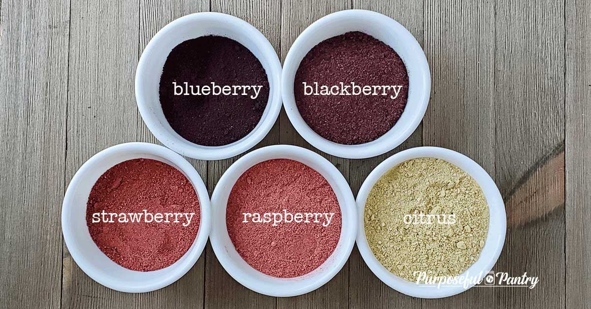 White bowls of various dehydrated fruit powders in different a rainbow of colors on a wooden background