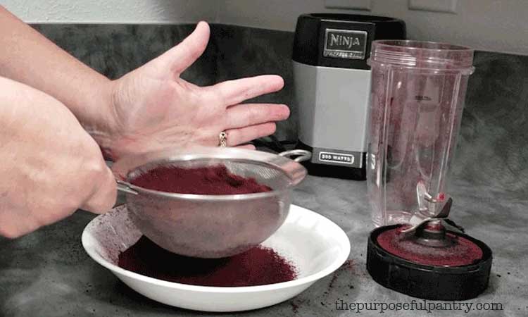 Person sifting blueberry powder through a strainer to remove seeds.