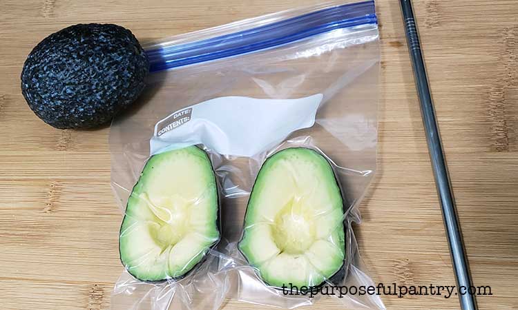a fresh avoado with a freezer bag of avocado halves and a stainless steel straw to show how to remove air manually