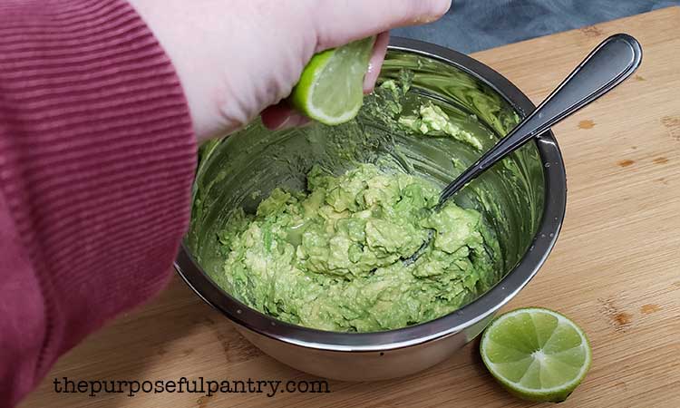 Squeezing lime juice into a stainless steel bowl of mashed avocado to help preserve it
