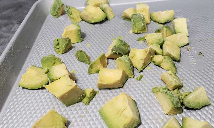 chunks of avocado on a stainless steel cookie sheet being prepared to be flash frozen