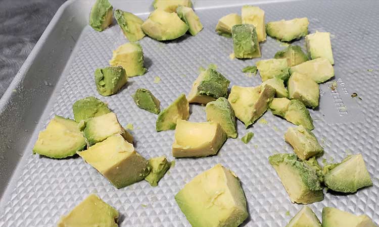 chunks of avocado on a stainless steel cookie sheet being prepared to be flash frozen