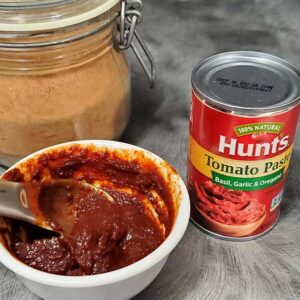 Tomato paste in a white dish with jar of tomato powder and can of tomato paste