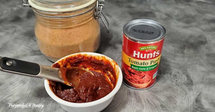 Tomato paste in a white dish with jar of tomato powder and can of tomato paste