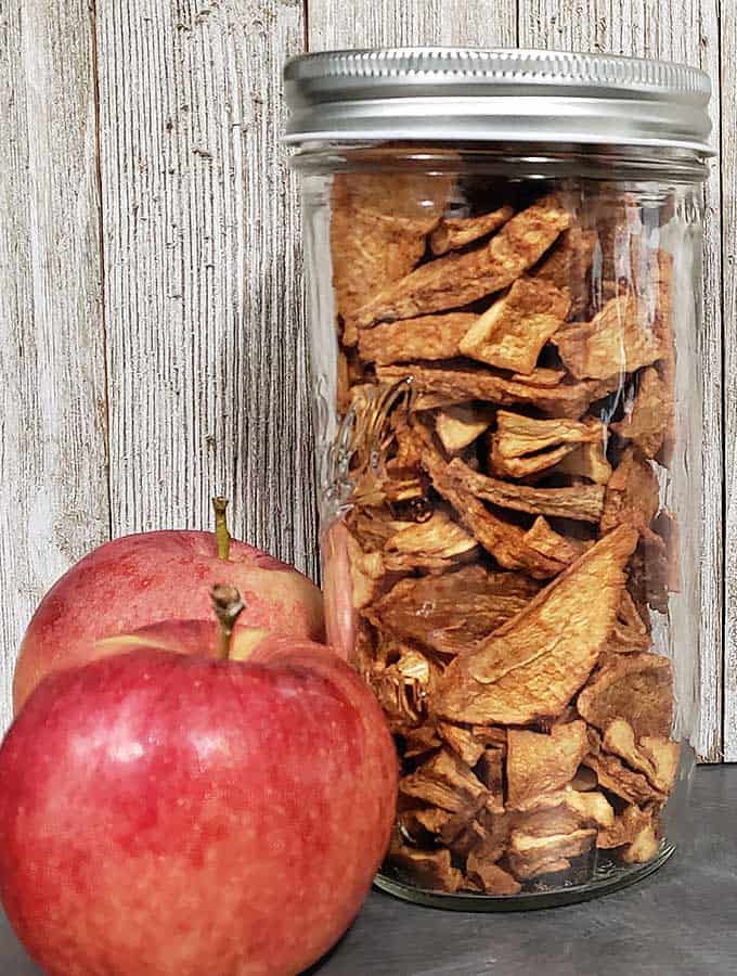 two apples with a jmason jar of dehydrated apple slices