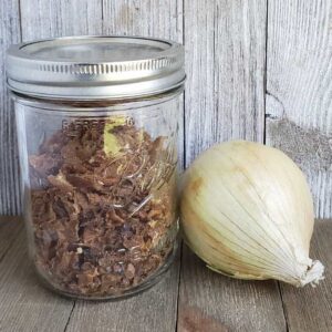 Mason jar of dehydrated caramelized onion with a fresh onion on a wooden surface