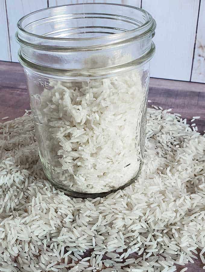 a mason jar of dehydrated rice for instant rice, and raw rice on a wooden cutting board.