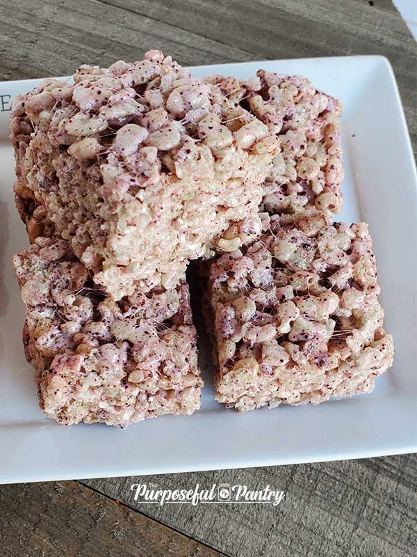 Blueberry rice krispies treats on a white serving dish set on a wooden background