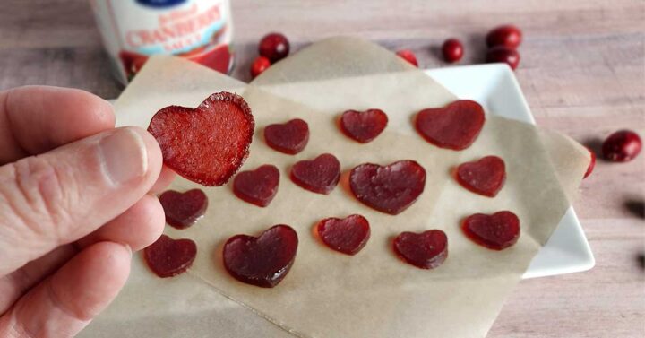Cranberry gummies on parchment paper with cranberry sauce can and scattered cranberries in the background.