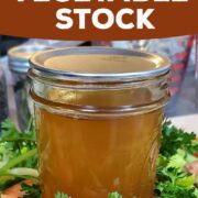 Canned jar of vegetable stock on a bed of fresh vegetables.