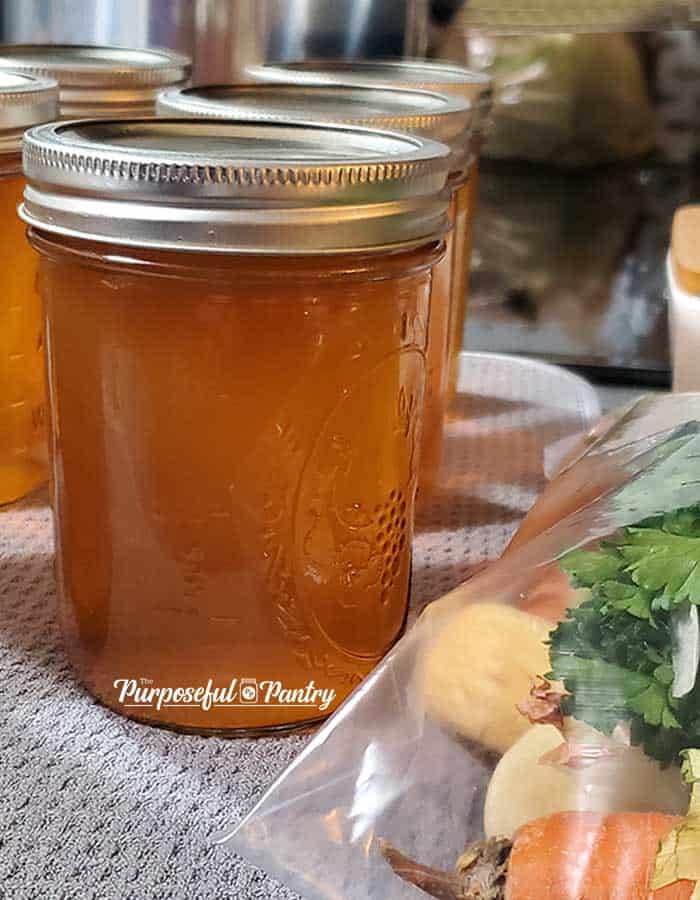 Canning jar of vegetable stock with fresh vegetable scraps in freezer bag in foreground