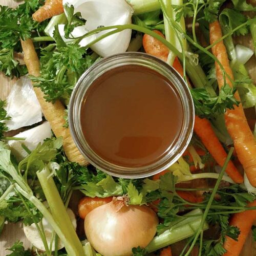 Top view of a jar of deep amber vegetable broth on a bed of fresh vegetables
