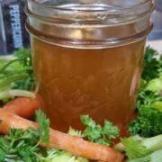 close up of a mason jar of amber colored vegetable broth on a bed of celery, parsley, carrots and parsnips