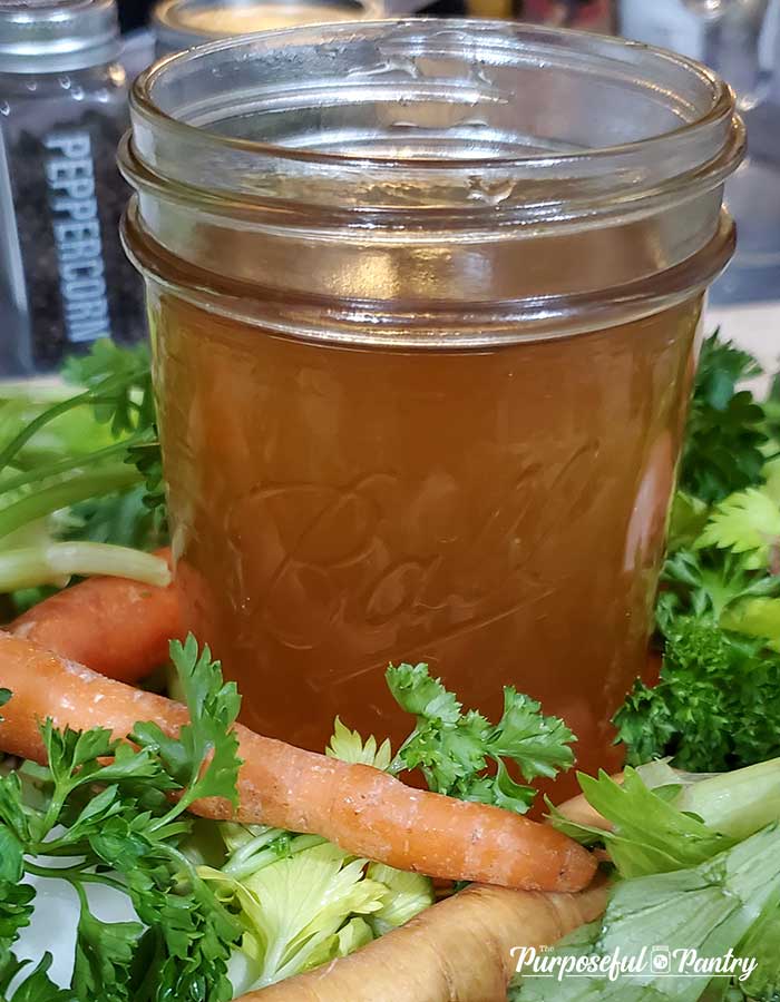 close up of a mason jar of amber colored vegetable broth on a bed of celery, parsley, carrots and parsnips