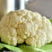 A head of fresh cauliflower in front of a large stockpot set on a green cloth
