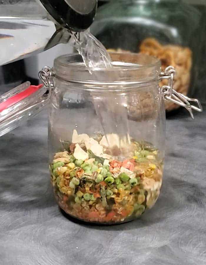 Glass clamp jar with water pouring into it to rehydrate the dehydrated vegetables indside
