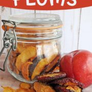 Dehydrated plums in a jar, on a wooden table, and a fresh plum for drying