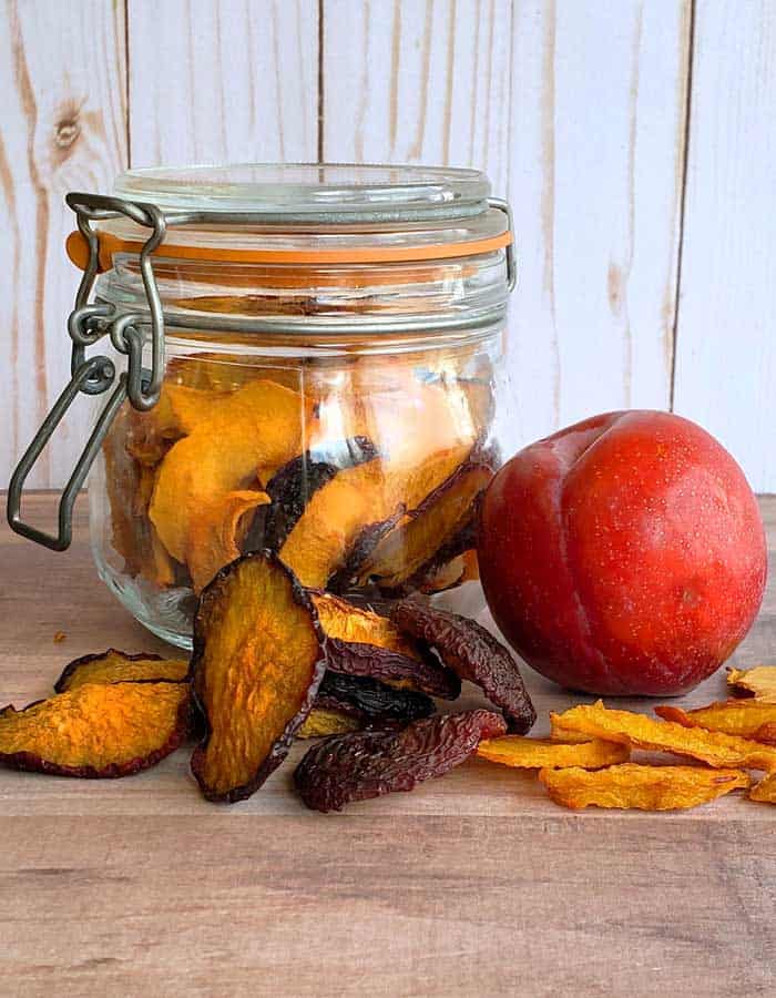 Dehydrated plums in a jar, on a wooden table, and a fresh plum for drying
