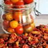 Glass jar of cherry tomatoes with dried tomatoes scattered around it