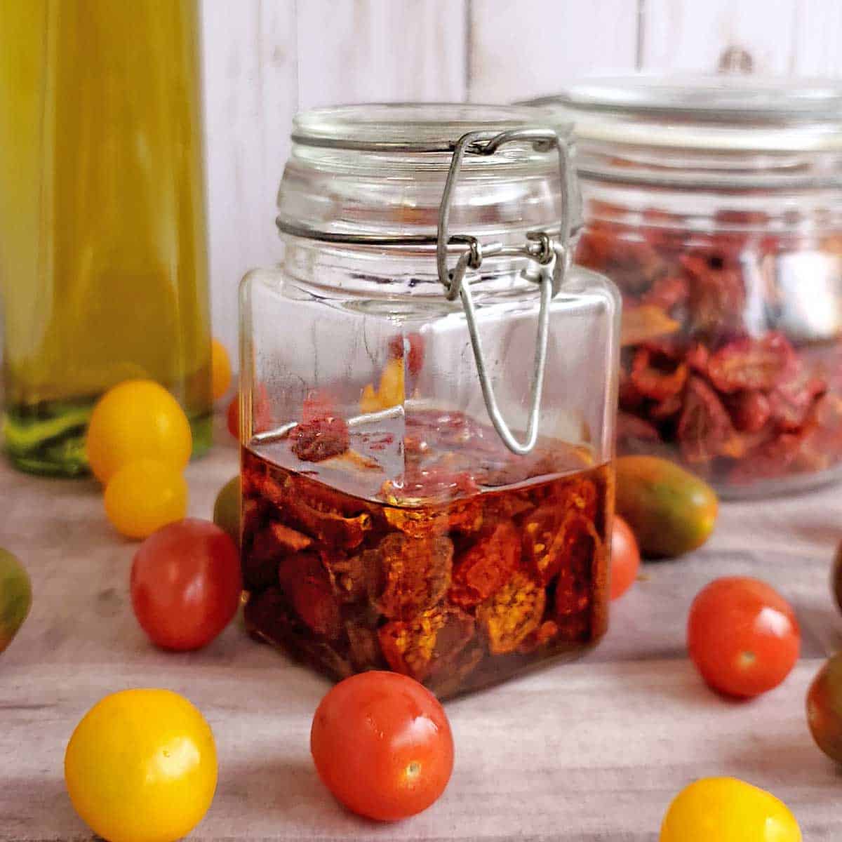 Jar of homemade sun dried tomatoes with olive oil and dried tomatoes in the background.