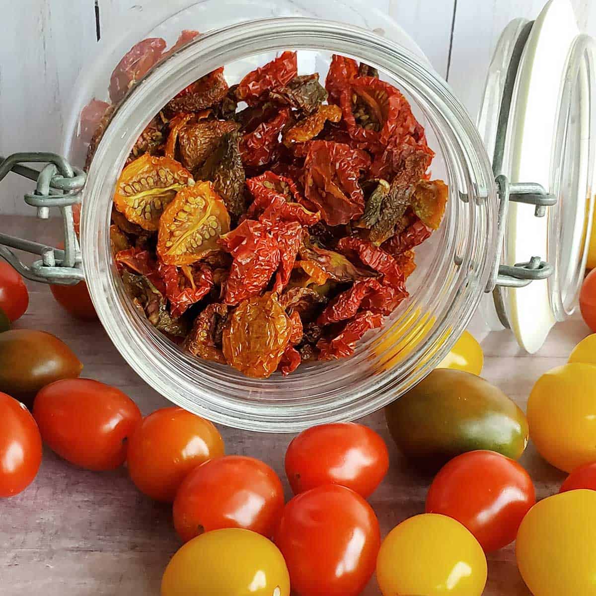 Jar of dehydrated cherry tomatoes spilling out to fresh cherry and grape tomatoes on table top