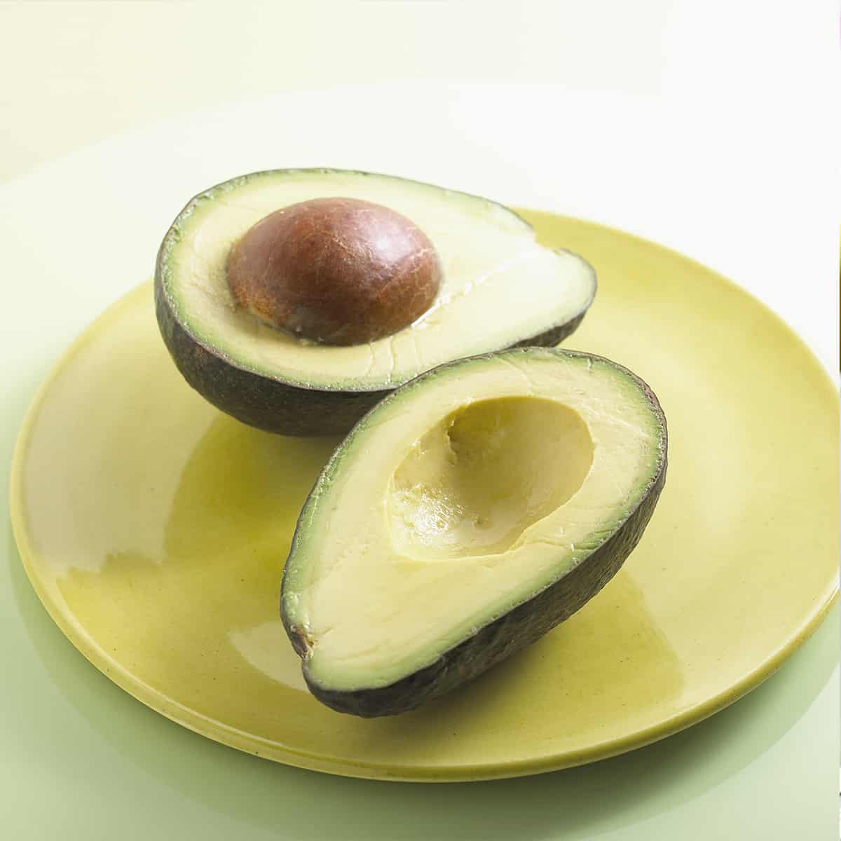 Halved avocado with seed on a yellow plate