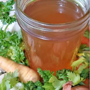 Vegetable stock about to be canned on a bed of fresh vegetables and herbs