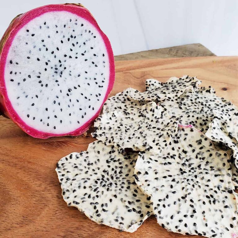 Fresh dragon fruit next to a pile of dehydrated dragon fruit (pitaya) chips on a wooden surface