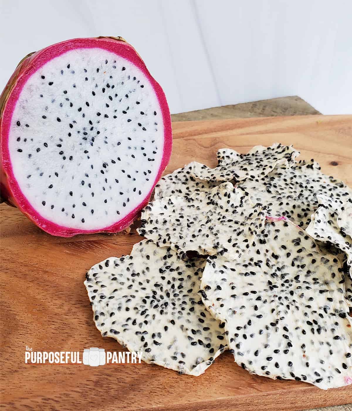 Fresh dragon fruit next to a pile of dehydrated dragon fruit (pitaya) chips on a wooden surface