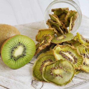 Fresh sliced kiwi with dehydrated kiwi slices falling out of a mason jar onto a white wooden surface