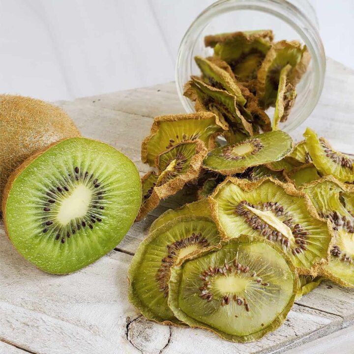 Fresh sliced kiwi with dehydrated kiwi slices falling out of a mason jar onto a white wooden surface
