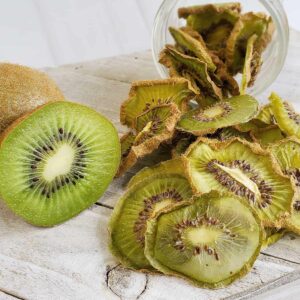 Fresh sliced kiwi with dehydrated kiwi slices falling out of a mason jar onto a white wooden surface