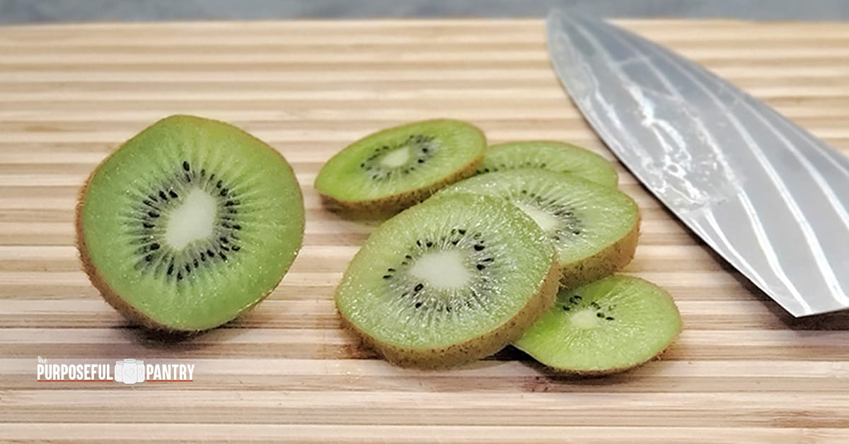 Sliced fresh kiwi on a wooden cutting board with a chef's knife