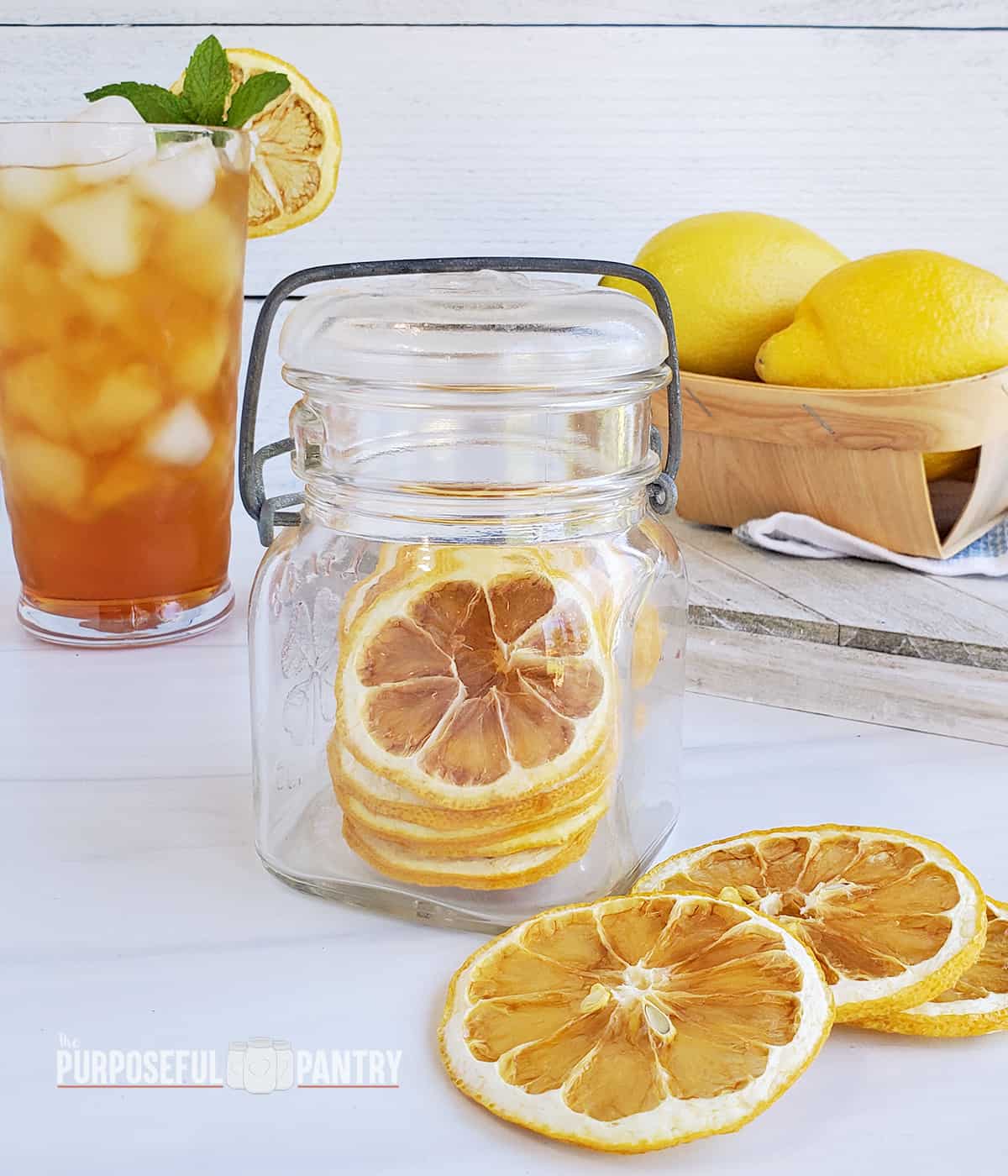 Dried lemon slices in a jar, on the table, and one in a glass of iced tea. and fresh lemons