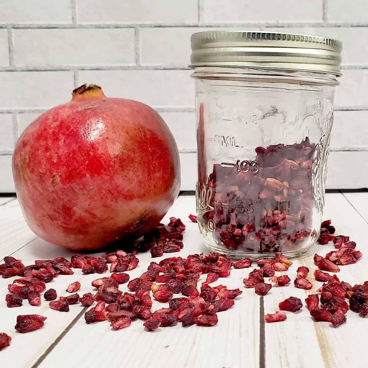 Pomegrate and jar of dehydrated pomegranate arils on white background